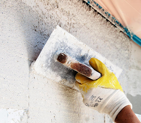 Hand mit Kelle verputzt eine Wand
